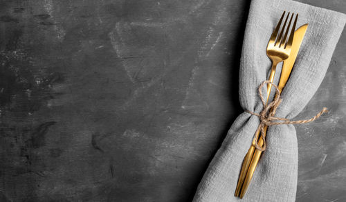 Golden cutlery fork and knife in grey napkin on dark grey shabby background. 