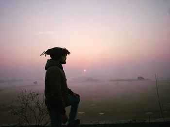 Side view of young man standing against sky during sunset