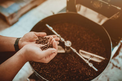 Cropped hands of man holding coffee beans while standing in shop