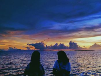 Rear view of couple on sea against sky during sunset