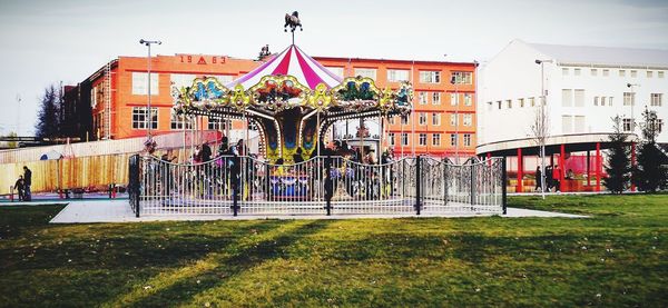 View of amusement park by buildings against sky