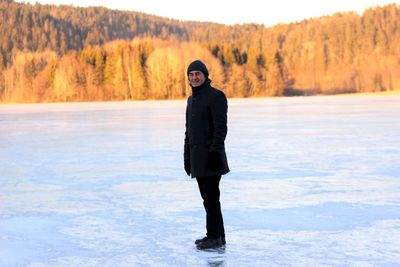 Smiling mid adult man standing on frozen lake against forest