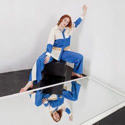 Fashion portrait of stylish woman in summer blue white stripes suit  sitting near reflecting mirror