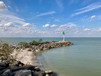 Lighthouse on rocks by sea against sky