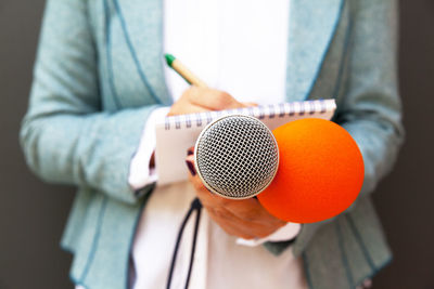 Midsection of journalist writing in book while holding microphones