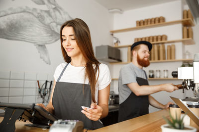 Portrait of young woman using mobile phone while standing in cafe