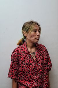 Young woman looking away while standing against wall