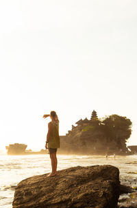 Man standing on rock looking at sea against sky