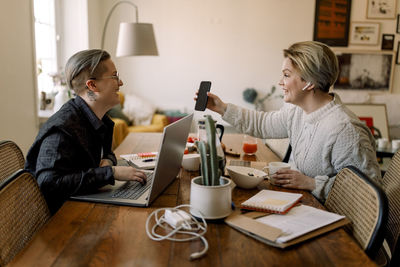 Happy lesbian couple sharing smart phone while working together at home