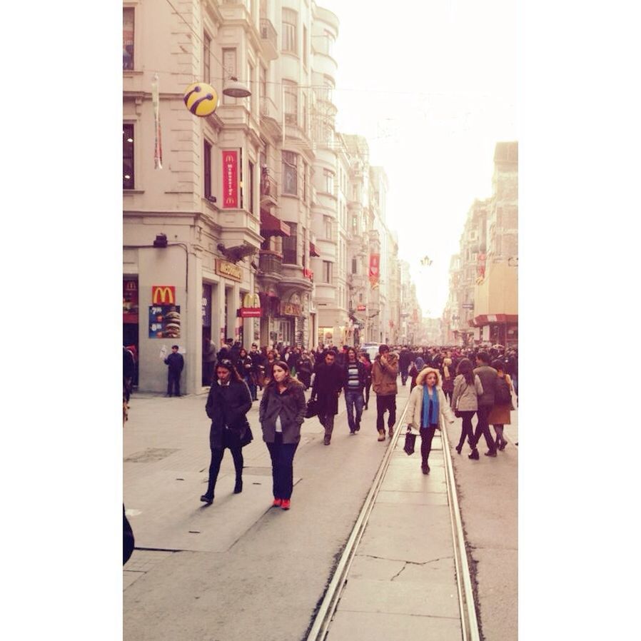 architecture, building exterior, built structure, large group of people, men, city, person, walking, street, city life, transfer print, lifestyles, auto post production filter, clear sky, mixed age range, city street, building, sunlight, group of people