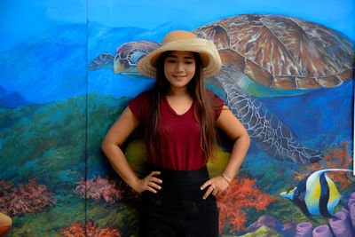 Woman in hat standing against mural