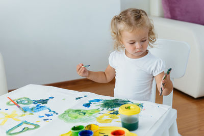 Toddler girl painting at home. happy creative child spending time with fun and joy. learning colours