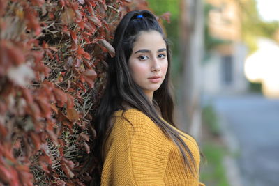 Portrait of young woman standing by plants outdoors