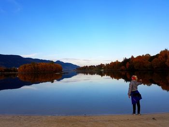 Woman standing by lake against blue sky