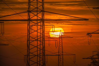 Low angle view of electricity pylon against sky during sunset