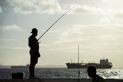 Man fishing on beach against sky