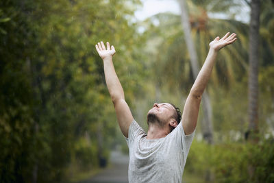 Rear view of man with arms outstretched standing against trees