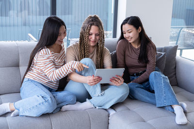 Friends using phone while sitting on sofa at home