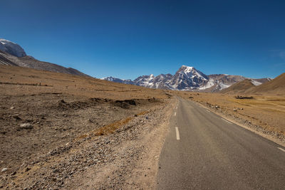 Road leading towards mountains against blue sky