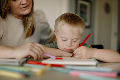 Boy with down syndrome drawing in book by mother at home