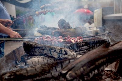 Cropped hands of men preparing meat on barbecue