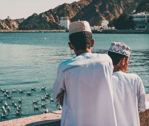 Rear view of men standing by sea against mountain