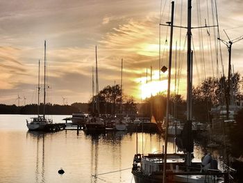 Sailboats moored at harbor against sky during sunset