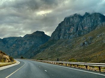 Road leading towards rocky mountains against sky