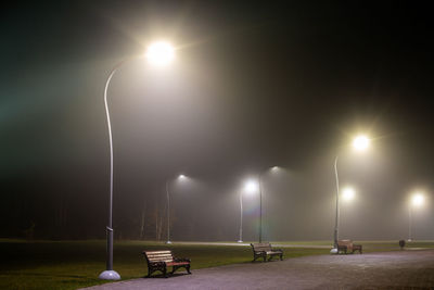 Illuminated street lights and empty benches at foggy night