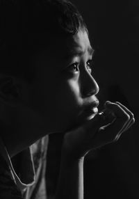 Close-up side view of young boy against black background