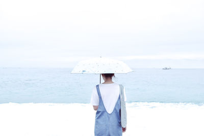 Rear view of woman standing at beach during winter