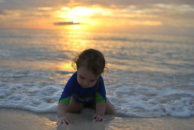 Girl playing with water at beach against sky during sunset