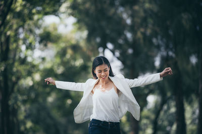 Woman with arms outstretched standing against trees