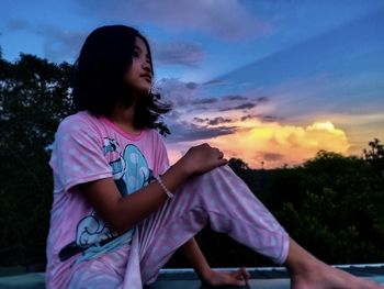 Young woman sitting in front of sky during sunset