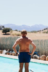 Rear view of shirtless man standing in swimming pool against sky