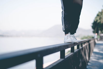 Low section of person standing on railing against sky