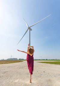 Rear view of woman dancing against windmill during sunny day
