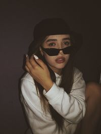 Portrait of young woman wearing sunglasses against black background