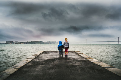 Rear view of kids standing on pier looking at sea