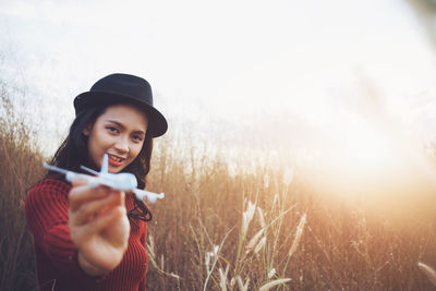 Portrait of smiling young woman holding model airplane while standing by plants