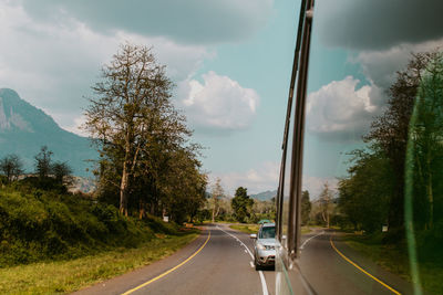 Cars on road by trees against sky