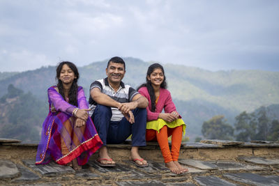 Indian father sitting with his daughters and smiling, happy family concept.