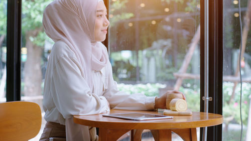 Woman holding cup while sitting on table at restaurant