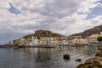 Cityscape by sea against cloudy sky 