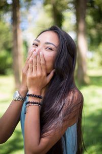 Portrait of young woman covering mouth while standing at park