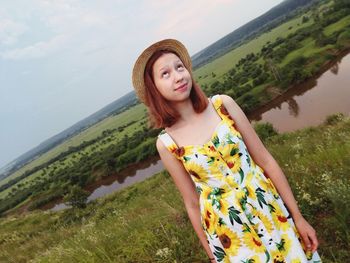 Young woman wearing hat looking up while standing on field