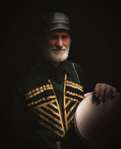 Portrait of man with drum standing against black background