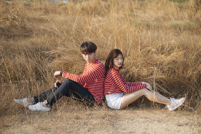 Couple sitting amidst grass on field