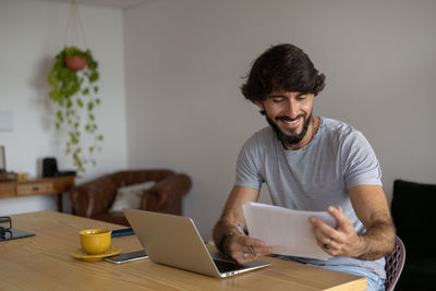 Man working at home in his kitchen with laptop and papers on wooden desk.  notebook . home office