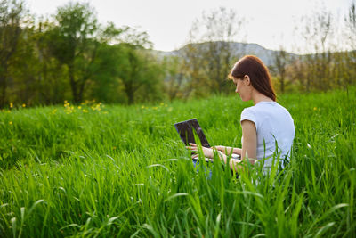 Rear view of woman using mobile phone while sitting on grassy field